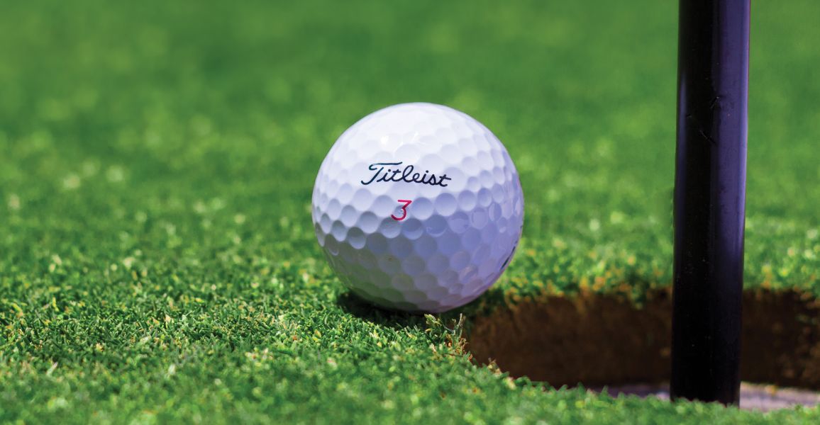 Titleist golf ball with a single number rolling into a golf hole