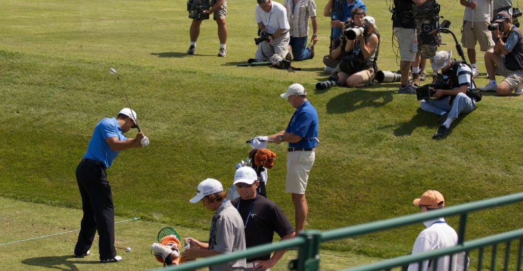 Pro golfer practising before his round with people taking pictures of him with cameras