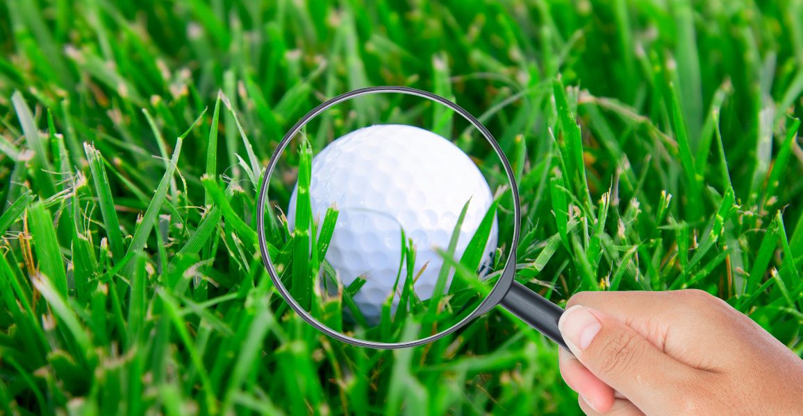 Golfer using a magnifying glass to search for a flyer lie