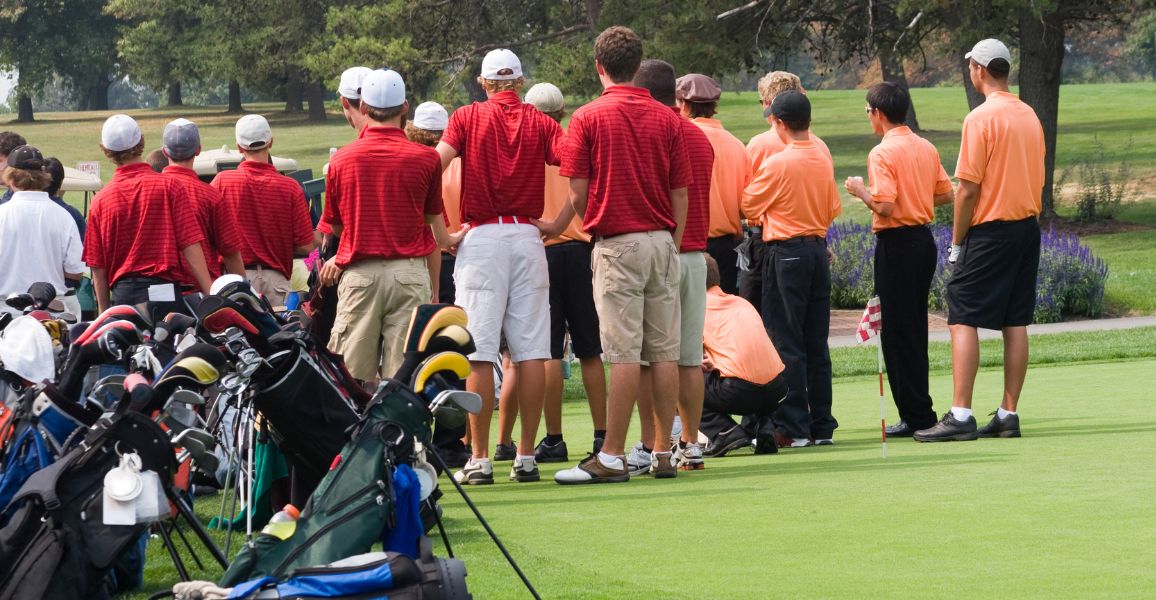 Two golf teams waiting by a green dressed in red and orange