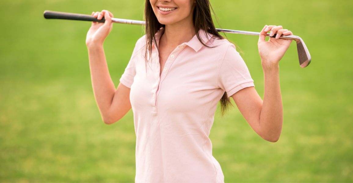 Woman smiling wearing a pink golf polo t-shirt with a golf club behind her back