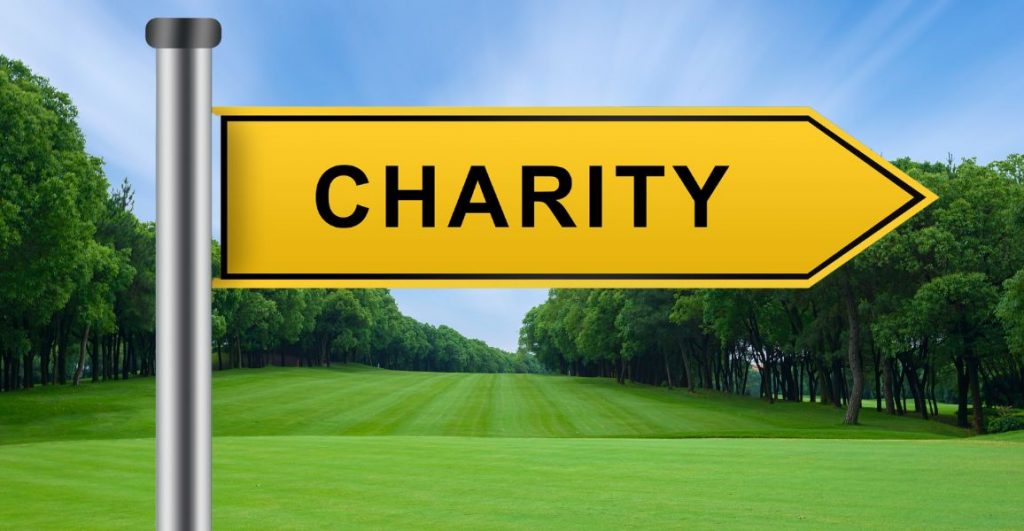 A yellow sign on a golf course pointing towards a charity golf tournament