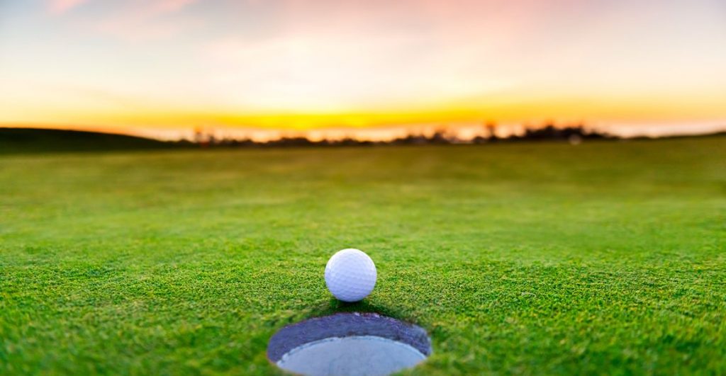 Golf ball about to roll into a hole on a putting green